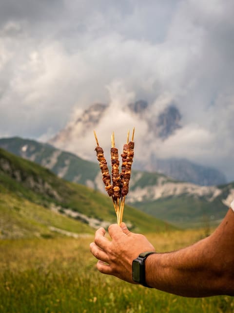 Arrosticini tenuti in mano davanti alle montagne abruzzesi
